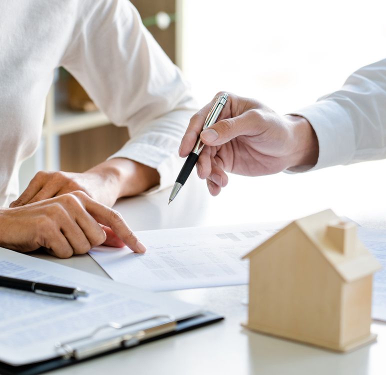 Hände, Papiere und ein Holzhaus auf dem Tisch